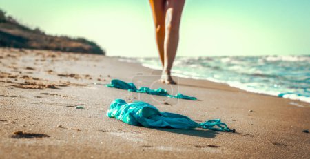 Téléchargez les photos : Maillot de bain dans le sable sur la plage près de la mer surf sur le fond d'une figure féminine nue et ciel bleu - en image libre de droit
