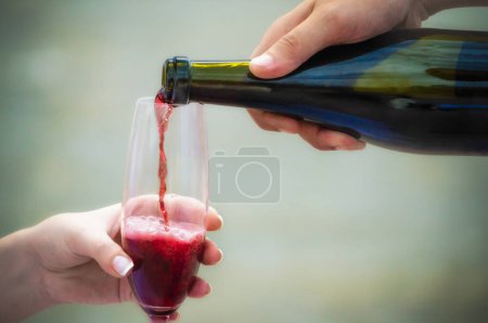Photo for Man pours red wine from a bottle into a glass in a woman's hand close up - Royalty Free Image
