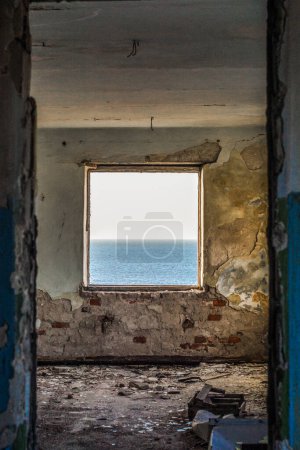 Téléchargez les photos : Horizon de mer dans la fenêtre de la salle minable détruite - en image libre de droit