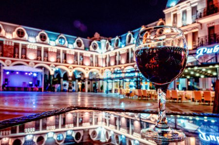 glass of red wine on a table with reflection in a cafe on an empty Piazza square in Batumi Georgia at night