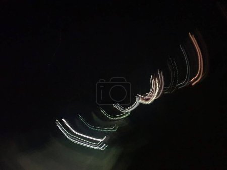 Photo for Moving lights have made made an abstract pattern of curved and dotted lines against a black sky. The lights are white, green and shades of pink. - Royalty Free Image