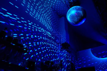 Discokugel reflektiert blaues Licht in dunkler Halle.