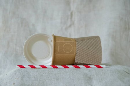 Foto de Portavasos biodegradable, tapa, taza, y beber paja en el fondo de lona de cáñamo. Bioware de papel y almidón de maíz. Copiar espacio. - Imagen libre de derechos