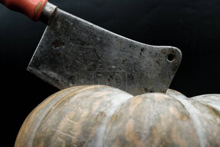 Téléchargez les photos : The ax stuck into the pumpkin. A gloomy invitation to a spooky party. - en image libre de droit