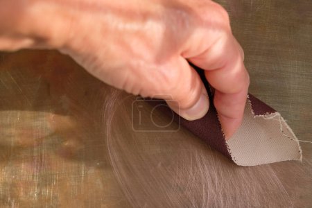 Téléchargez les photos : Main humaine avec du papier de verre sur fond de cuivre. Espace de copie. - en image libre de droit