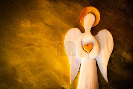 Foto de Una figura de madera de un ángel con un halo dorado. Corazón dorado. Imitación de fondo ardiente. Foto granulada. - Imagen libre de derechos