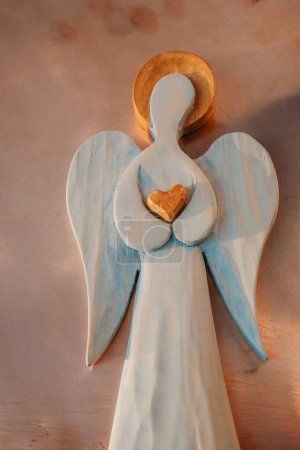 Foto de Una figura de madera de un ángel con un halo dorado. Corazón dorado. Melocotón pelusa color fondo. - Imagen libre de derechos