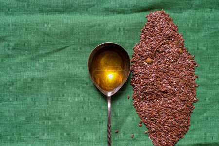 Flax seeds. Spoon filled with linseed oil. Green background. Copy space.