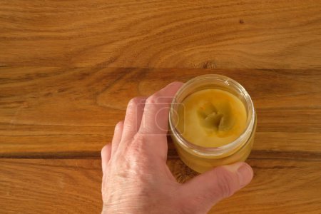 La mano de una mujer. Revestimiento protector de cera para muebles de madera en el frasco de vidrio. Superficie de mesa. Vista superior.