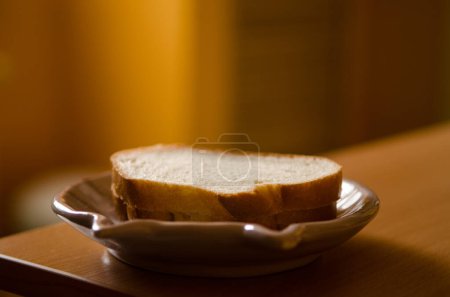 Photo for Two pieces of white bread lie on a saucer on a table in a yellow room with dimmed light, there is a copyspace - Royalty Free Image
