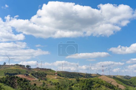 Foto de Las turbinas eólicas en la cima de la colina de hierba debajo del grupo de nubes blancas y el cielo azul en un día soleado, produjeron electricidad a partir de energía pura. - Imagen libre de derechos