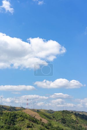 Foto de Las turbinas eólicas en la cima de la colina de hierba debajo del grupo de nubes blancas y el cielo azul en un día soleado, produjeron electricidad a partir de energía pura. - Imagen libre de derechos