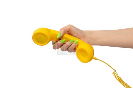 Foto de Auricular amarillo en mano de mujer con uñas verdes aisladas sobre un fondo blanco. Copiar espacio. - Imagen libre de derechos
