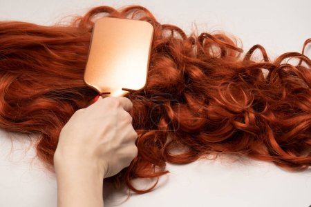 Rote lockige Haare in Frauenhänden mit roten Nägeln. Top0-Ansicht.