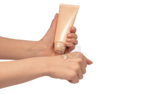 Beige cream tube in woman hands isolated on a white background. Cream swatch on woman hand.  Skin care concept.