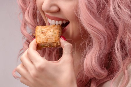 Photo for Woman with pink curly hair is eating baklava close-up. - Royalty Free Image