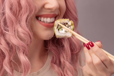 Photo for Young woman with red nails and pink hair is eating sushi close up. - Royalty Free Image