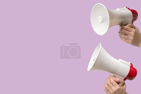 Megaphone in woman hands on a lilac background.  Copy space. 