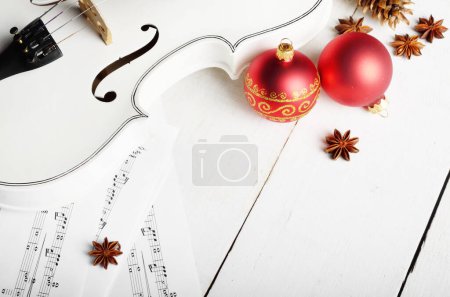 Photo for Close view of a violin musical notes and christmas decoration balls on white wooden table - Royalty Free Image