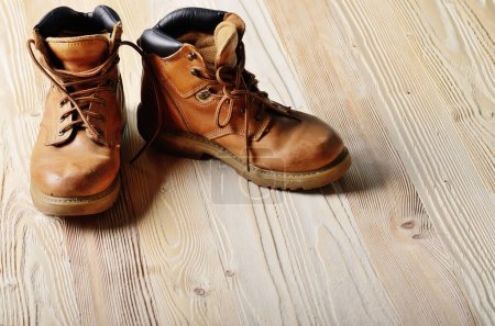 Yellow leather used work boots on wooden background closeup. Place for text