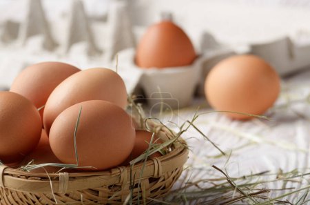 Foto de Huevos crudos de pollo marrón orgánico en canasta cuadrada de mimbre en mesa de madera de cocina blanca - Imagen libre de derechos
