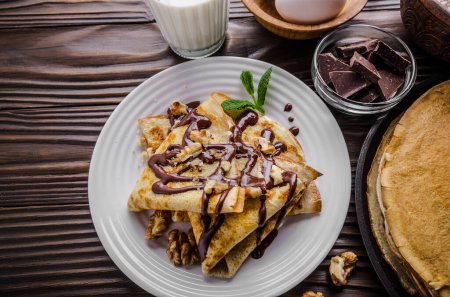 French crepes with chocolate sauce walnuts eggs and flour on wooden kitchen table