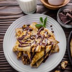 French crepes with chocolate sauce walnuts eggs and flour on wooden kitchen table