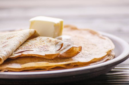 Stack of French crepes with butter in ceramic dish on wooden kitchen table