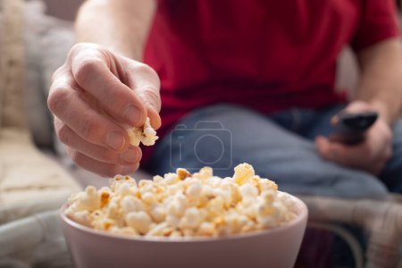 Caucasian man sitting on sofa with popcorn and tv remote
