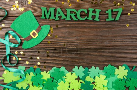 Photo for Happy Saint Patrick's mockup of handmade felt hat shamrock clover leaves and faux gold coins on wooden background - Royalty Free Image