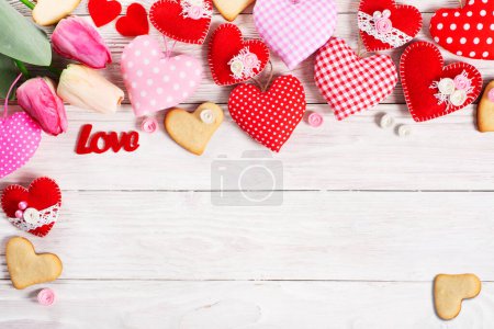 Foto de Corazones de tela de San Valentín cosidos a mano con tulipanes y galletas planas ponen fondo sobre mesa de madera blanca - Imagen libre de derechos