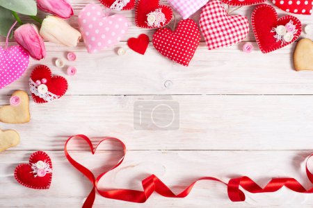 Foto de Corazones de tela hechos a mano cosidos tulipanes cinta y galletas para el día de San Valentín sobre fondo de madera blanca con espacio para copiar - Imagen libre de derechos