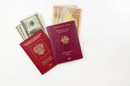 Offizielle deutsche und russische Pässe mit amerikanischen Dollars und Euro-Banknoten auf weißem Hintergrund