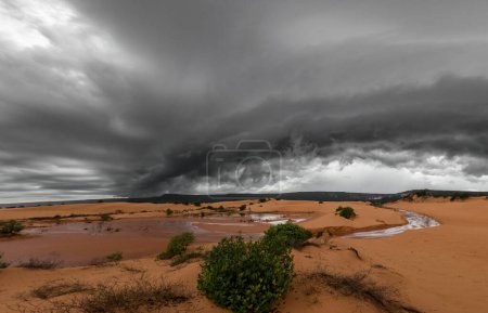 Une tempête puissante avec des nuages noirs s'élève au-dessus d'un paysage de sable et de dunes désolé, lointain et sombre.