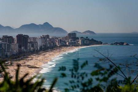 Téléchargez les photos : Coup d'oeil exclusif à Ipanema Beach, Rio, obscurci par une flore verdoyante, mettant en valeur le contraste nature-urbain. - en image libre de droit