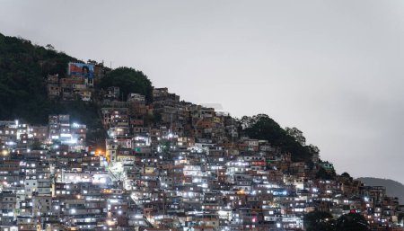Téléchargez les photos : Des maisons de favela éclairées couvrent une colline dans une ville brésilienne, créant une scène nocturne animée. - en image libre de droit