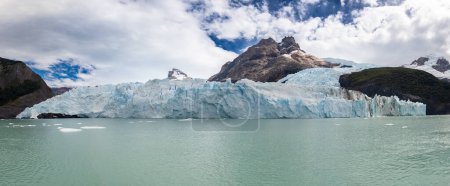 Gletscherfront und Berge spiegeln sich im ruhigen Wasser unter bewölktem Himmel.