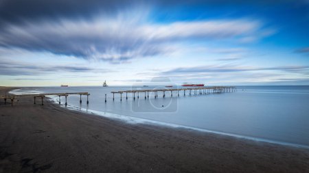 Foto de Mar tranquilo con muelle en descomposición capturado en larga exposición bajo nubes dinámicas. - Imagen libre de derechos