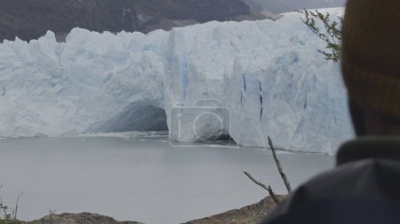 Tourist admires Perito Moreno Glaciers immense ice walls from behind, captured in a photo.