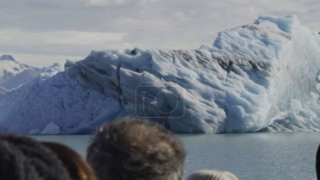 Tourists on a boat admire a large blue iceberg.