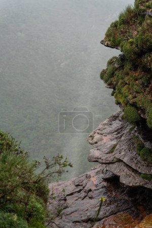 Foto de Una parte superior de las cascadas es soplada por vientos, formando una cortina brumosa sobre un valle verde. - Imagen libre de derechos