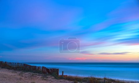 Strandszene bei Sonnenuntergang mit rosa und blauem Himmel, lange Belichtung für seidiges Wasser und flauschige Wolken.