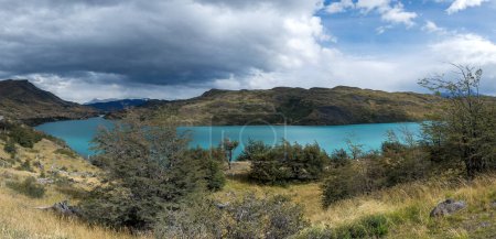 Turquoise lake amidst rugged landscape under cloudy skies.