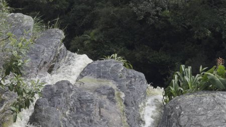 Slow-mo-Luftbild von Wasser, das von einem grünen Wasserfallgipfel fällt.