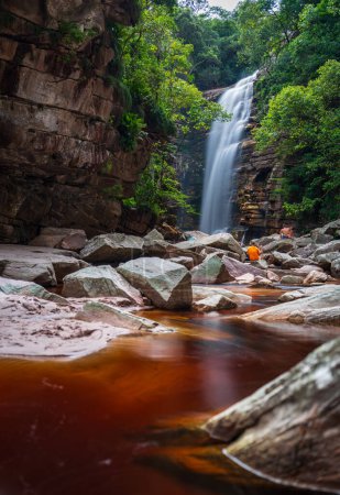 Individuell in Orange an einem ruhigen Wasserfall inmitten ruhiger Natur.