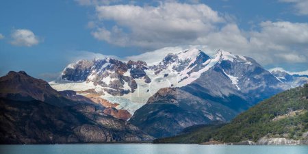 Faszinierender Gletscher eingebettet zwischen schroffen Gipfeln neben einem ruhigen, spiegelglatten See.