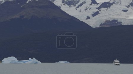 Cruceros en barco turístico entre icebergs masivos en lago tranquilo, capturado en slo-mo con espacio para el texto.