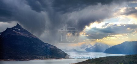 Dramatic glacier view with a mountain and dark clouds parting for sunlight.