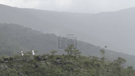 Unidentifiable hikers in white raincoats trek on a foggy mountain ridge during heavy rain.