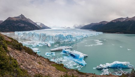 Glacier panorama with icebergs in tranquil mountain setting.